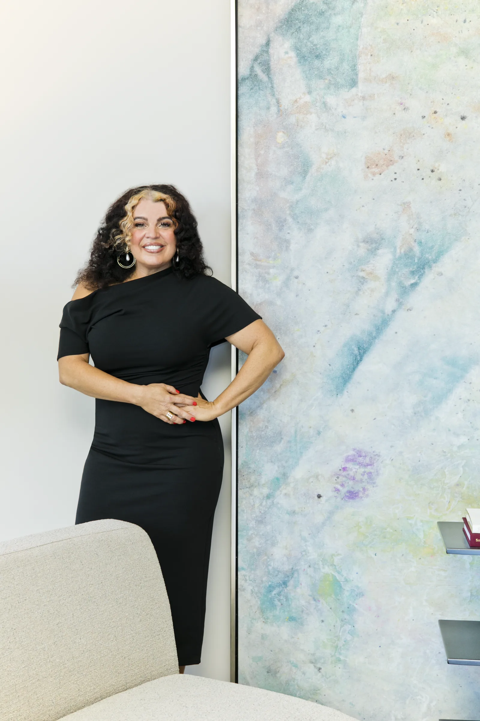 Katina Benenate smiling in a black dress beside a large abstract painting