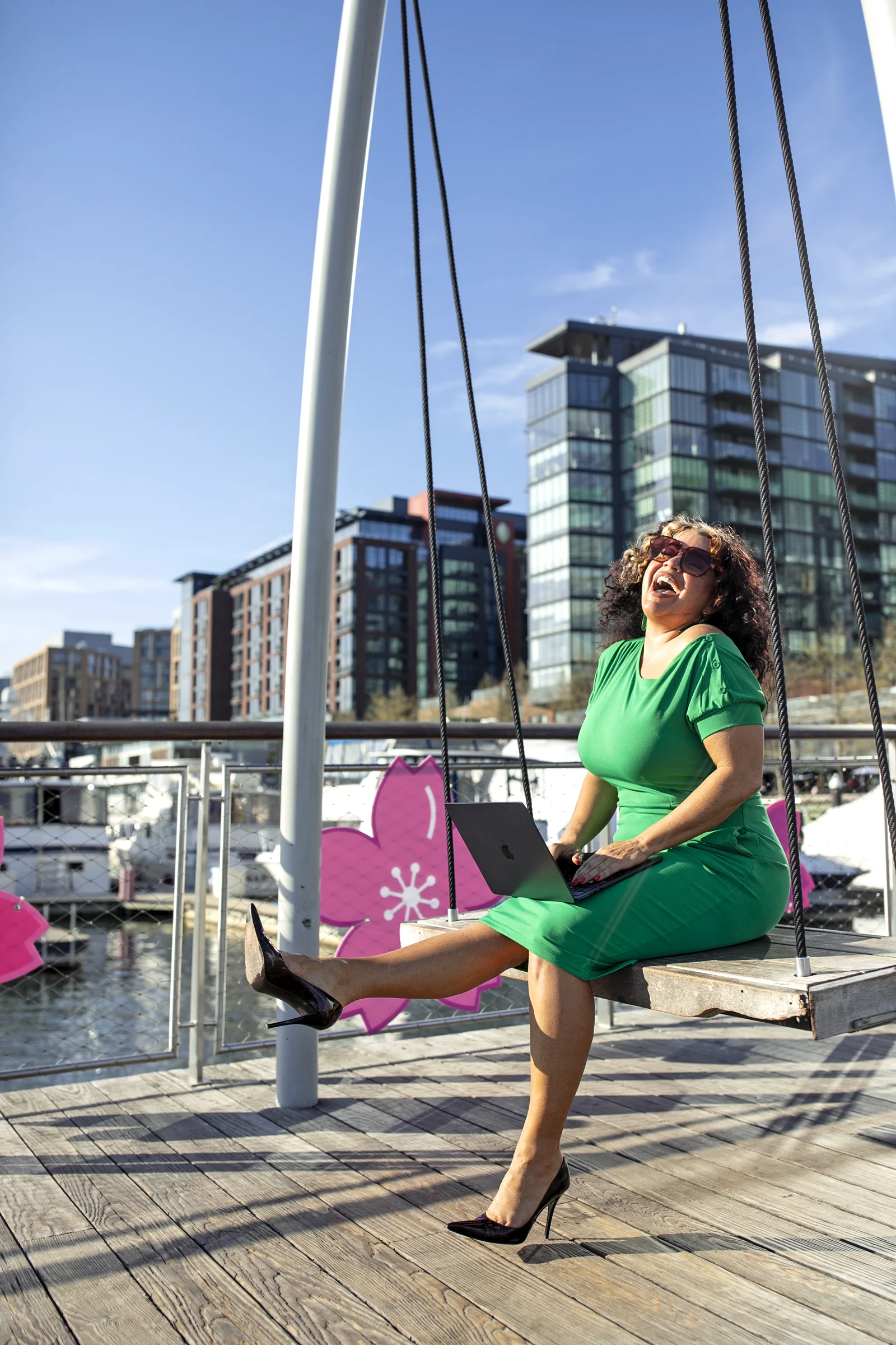 House of Benenate Realtor laughing on a waterfront swing in a green dress