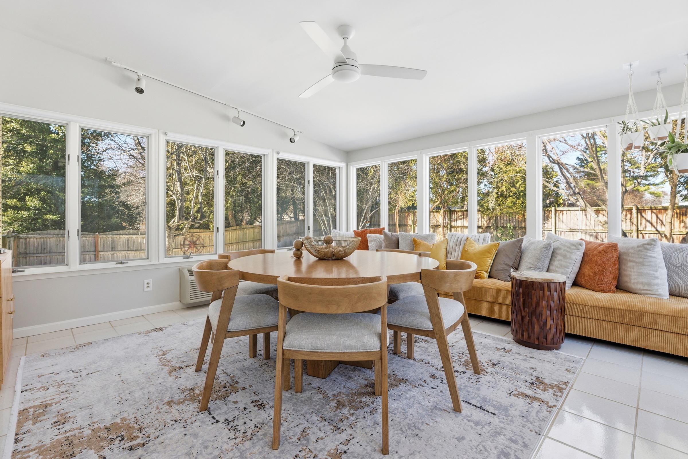 Light-filled sunroom with a dining table, wraparound windows, and warm layered furnishings